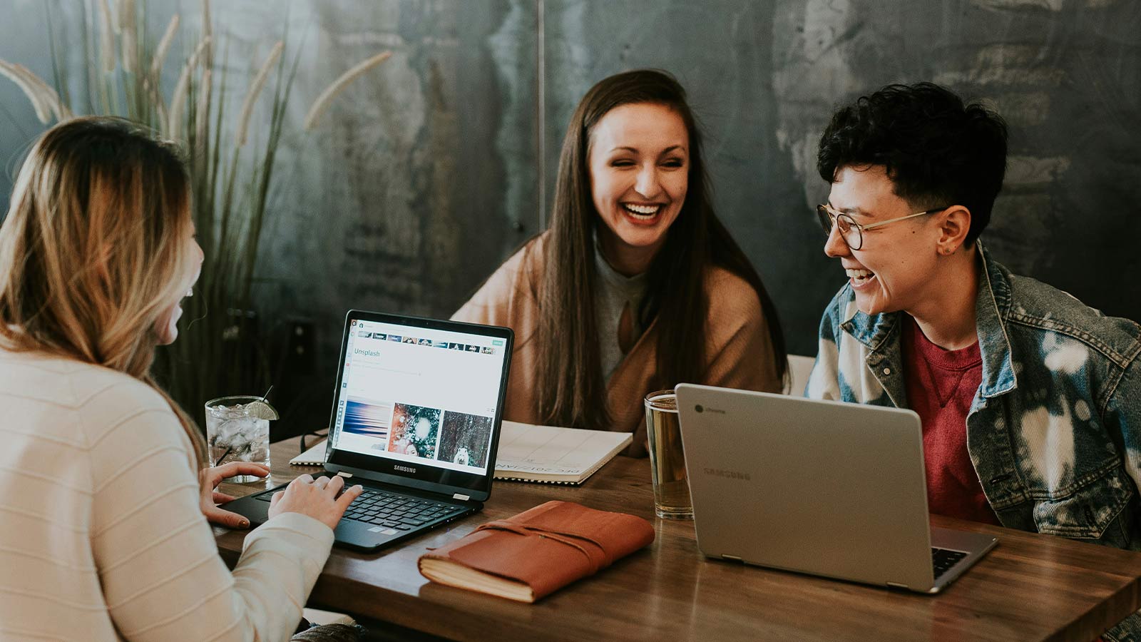 Three people working together on laptops at a shared table in a bright cafe