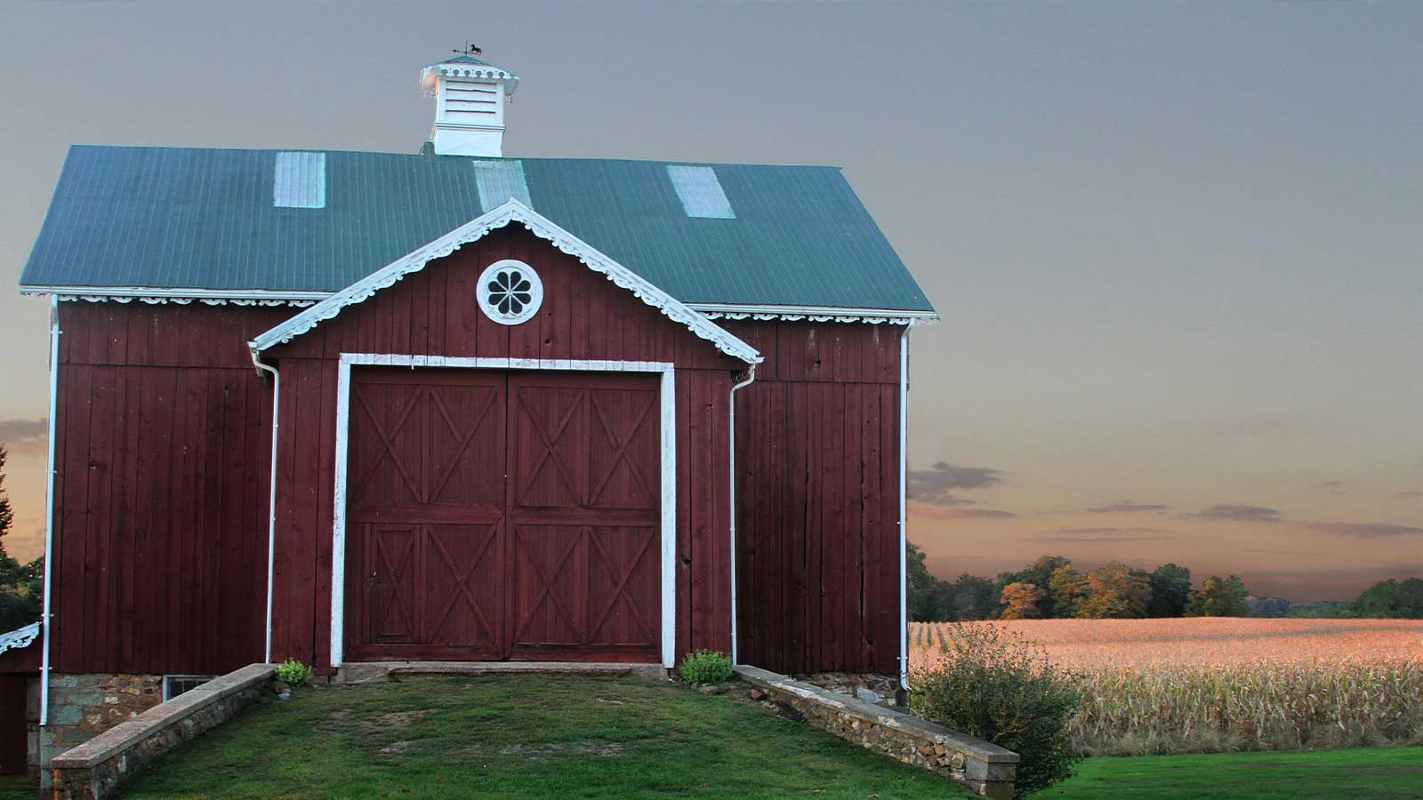 A red barn with a cupola beside a cornfield at dusk in rural Maryland
