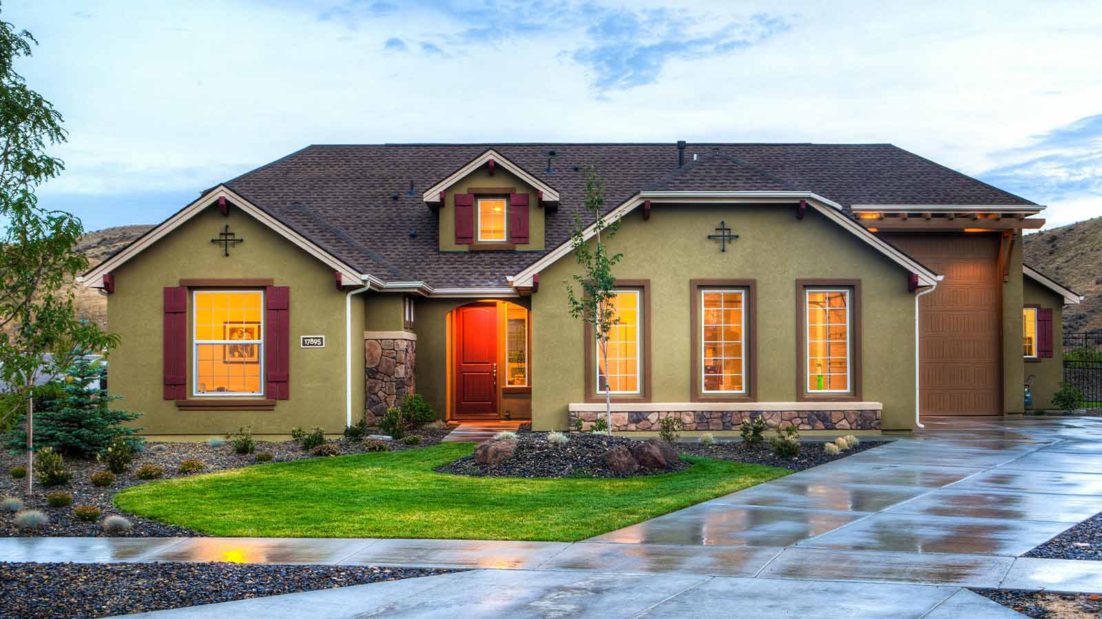 Stucco craftsman style house with a lit entry at dusk below dry foothills