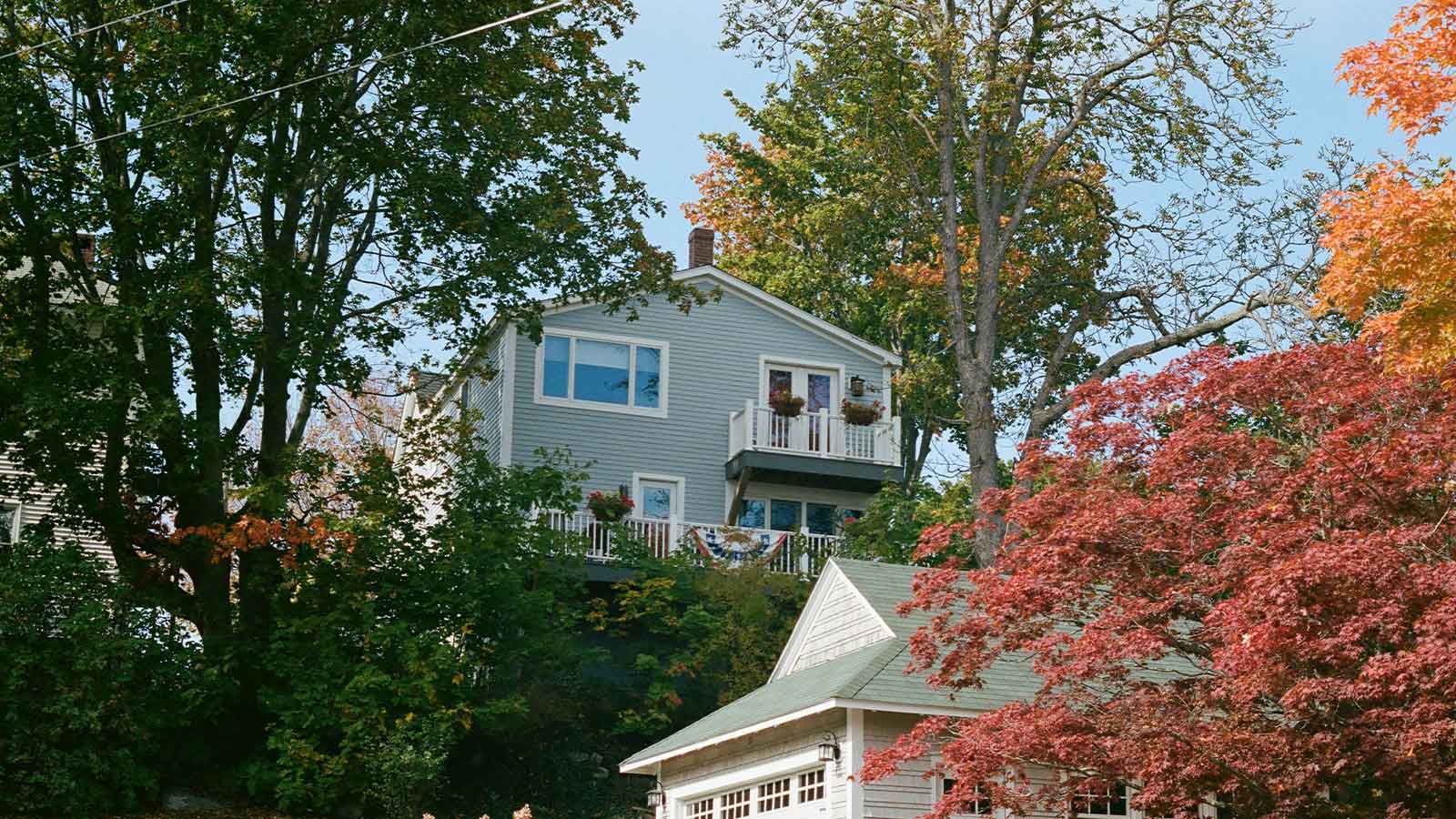 Two story clapboard house on a wooded hillside surrounded by maple trees in autumn color