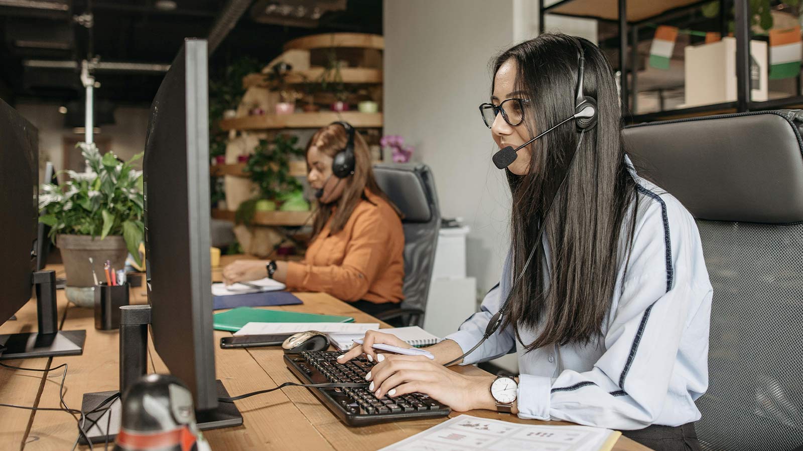 A research specialist in a headset working at a desk of monitors in an open office