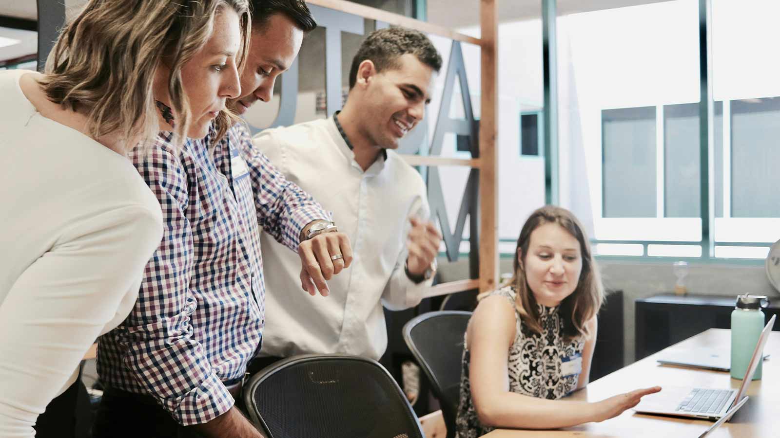 A team gathered around a laptop in an open plan office reviewing a document together