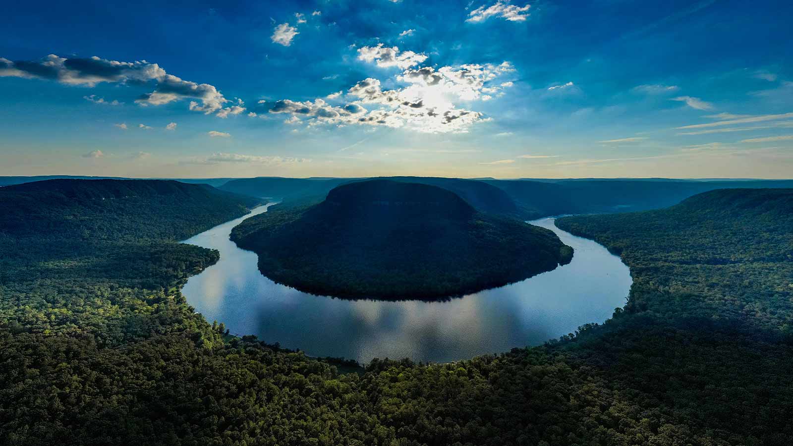 An aerial view of a wide river looping around a forested ridge in the Tennessee hills at dusk
