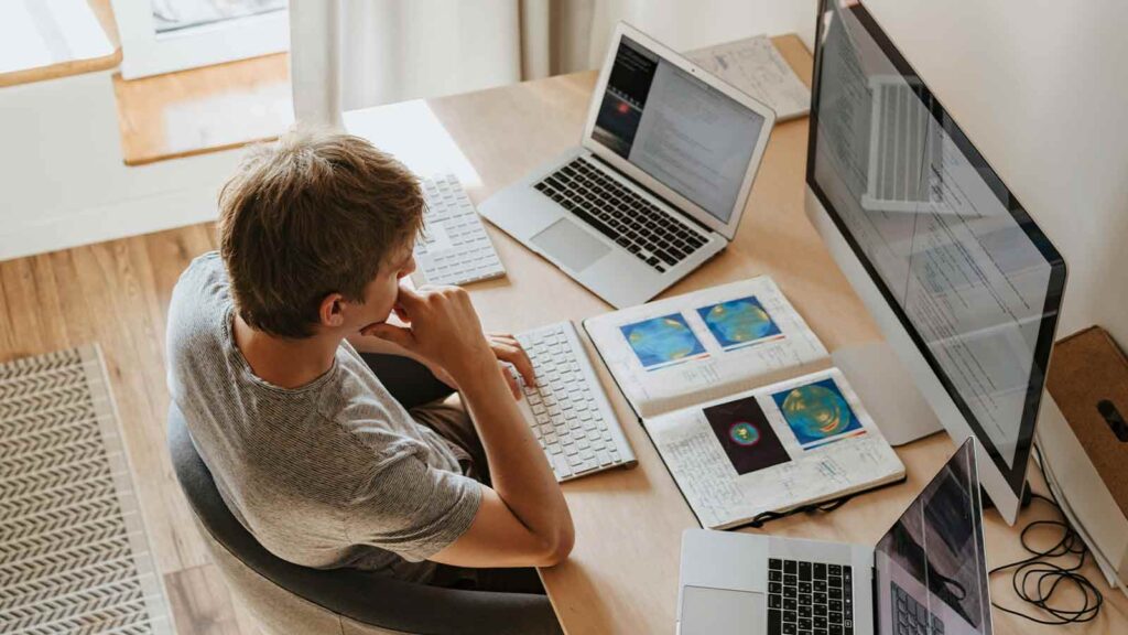 a man sitting at a desk with laptops and a book North Dakota Title Search