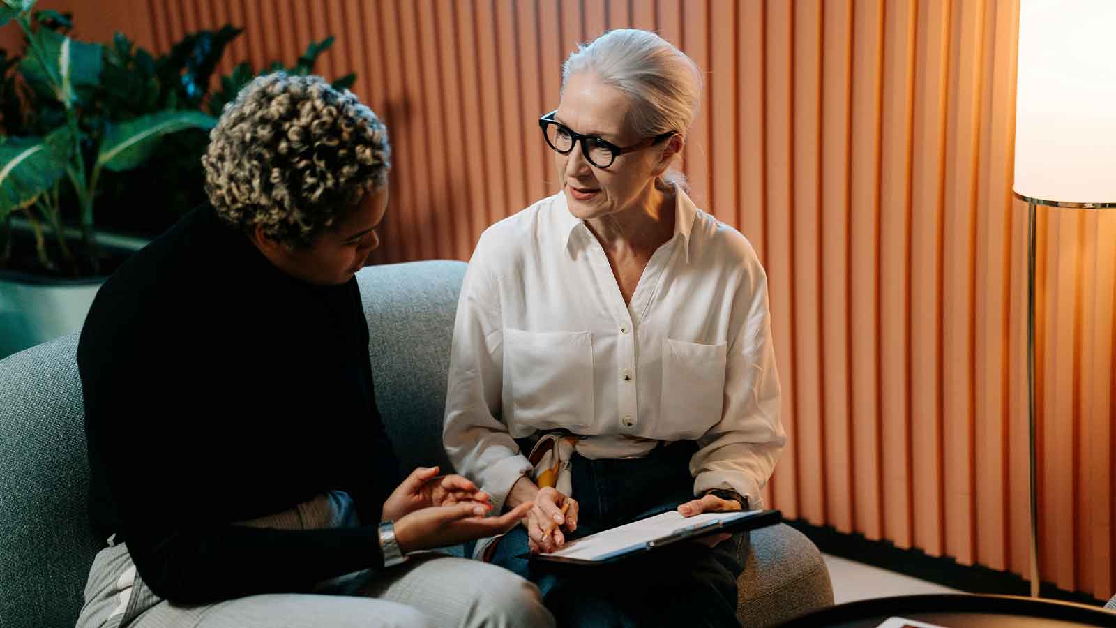 Two people seated on a couch reviewing a document on a clipboard in a warm office