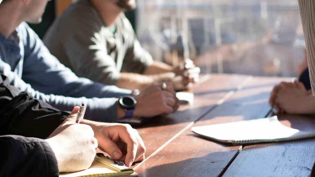 a group of people sitting at a table writing Property Searches