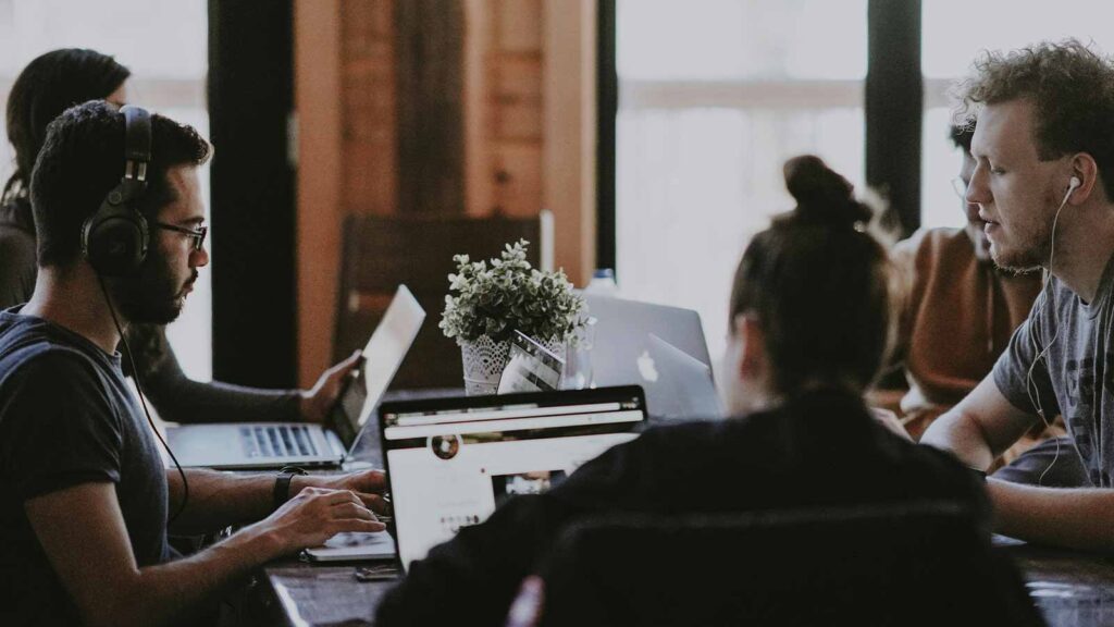 a group of people sitting at a table with laptops ai title search