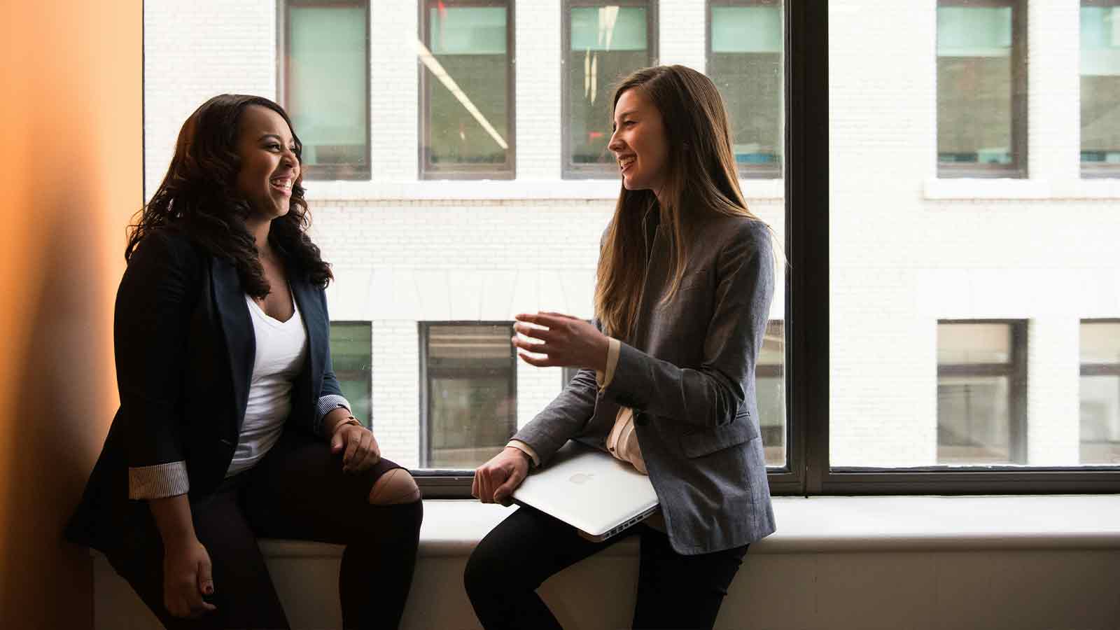 Two women engaged in conversation indoors. AI Compliance bloga