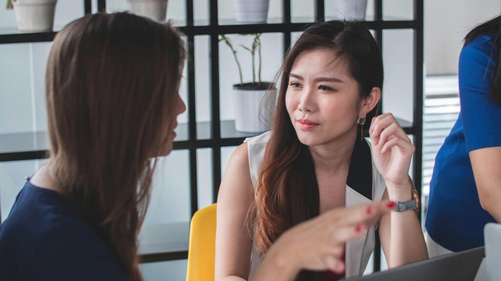 Two women discussing in an office. AI Title Clearance