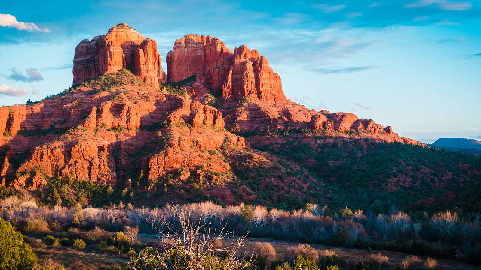 Red sandstone buttes rising above a wooded valley in Arizona under a blue sky at golden hour