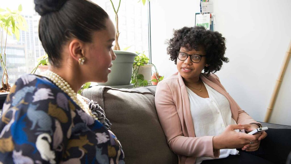 Two women engaged in conversation indoors. AI Title Search in Oregon