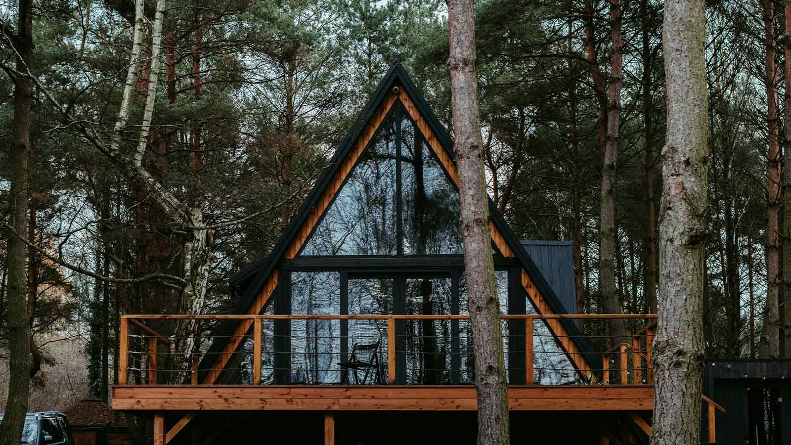 A timber and glass A-frame cabin with a deck set among tall pine trees