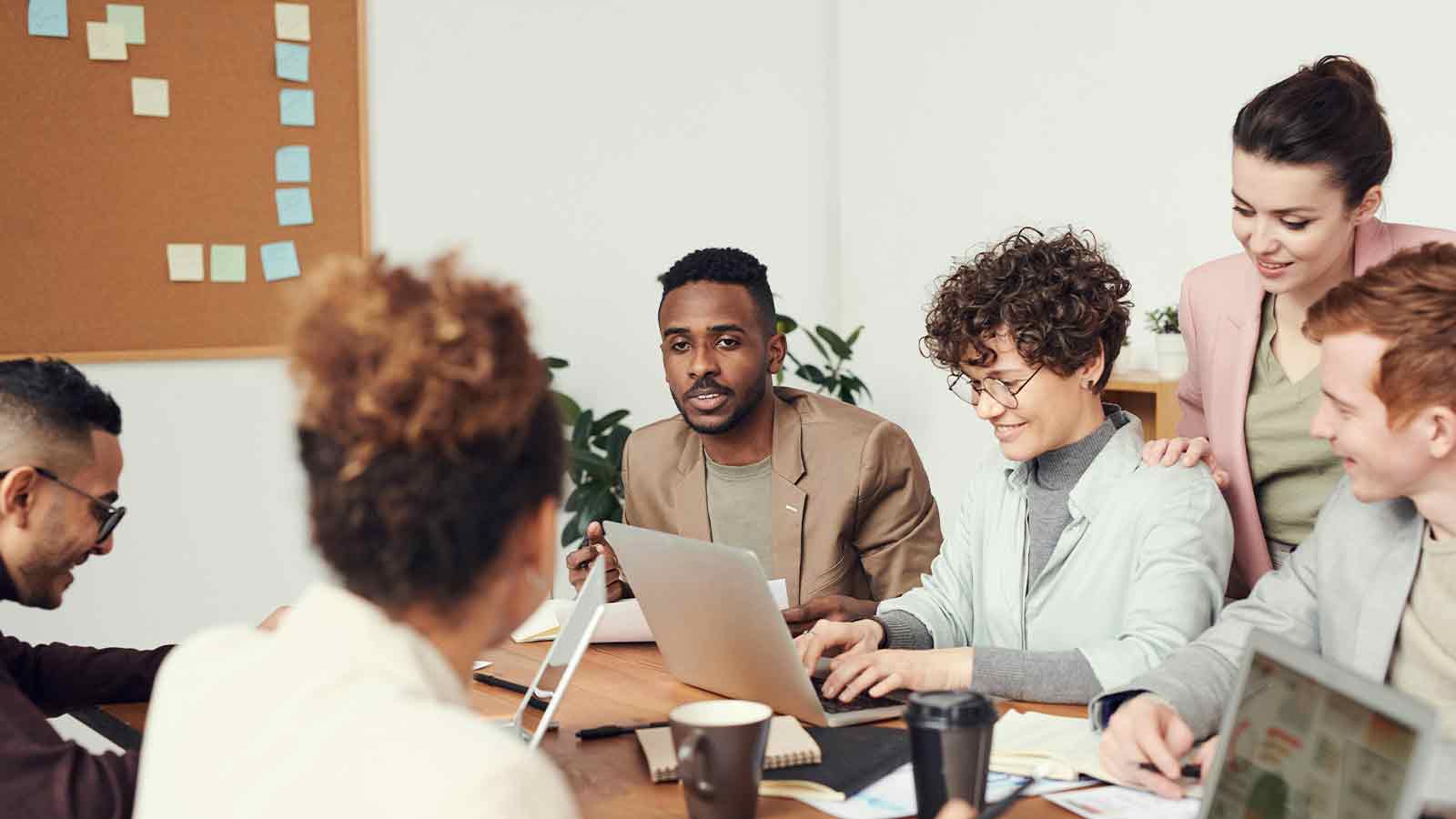 Colleagues gathered around a conference table reviewing a laptop in a bright office