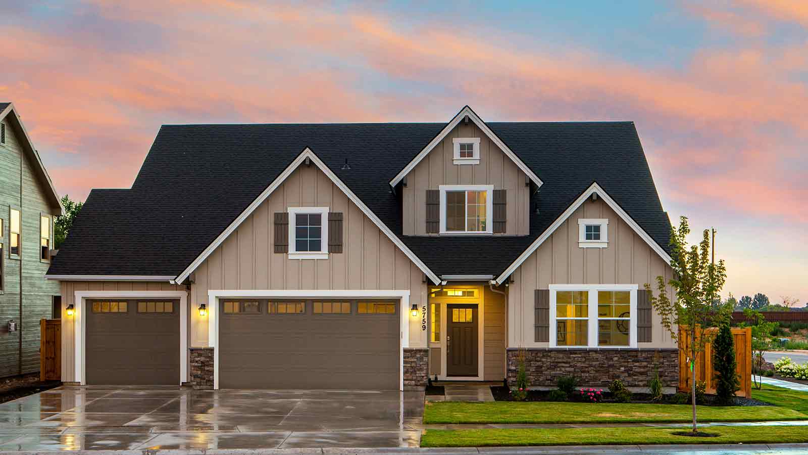 A newly built two story suburban house with a three car garage at dusk under a pink sky