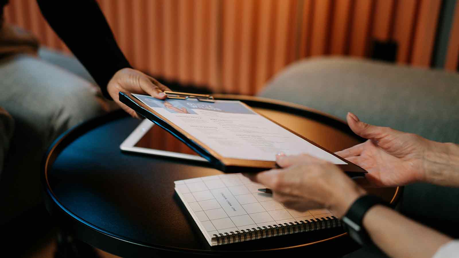 Hands passing a clipboard with a printed document across a low table